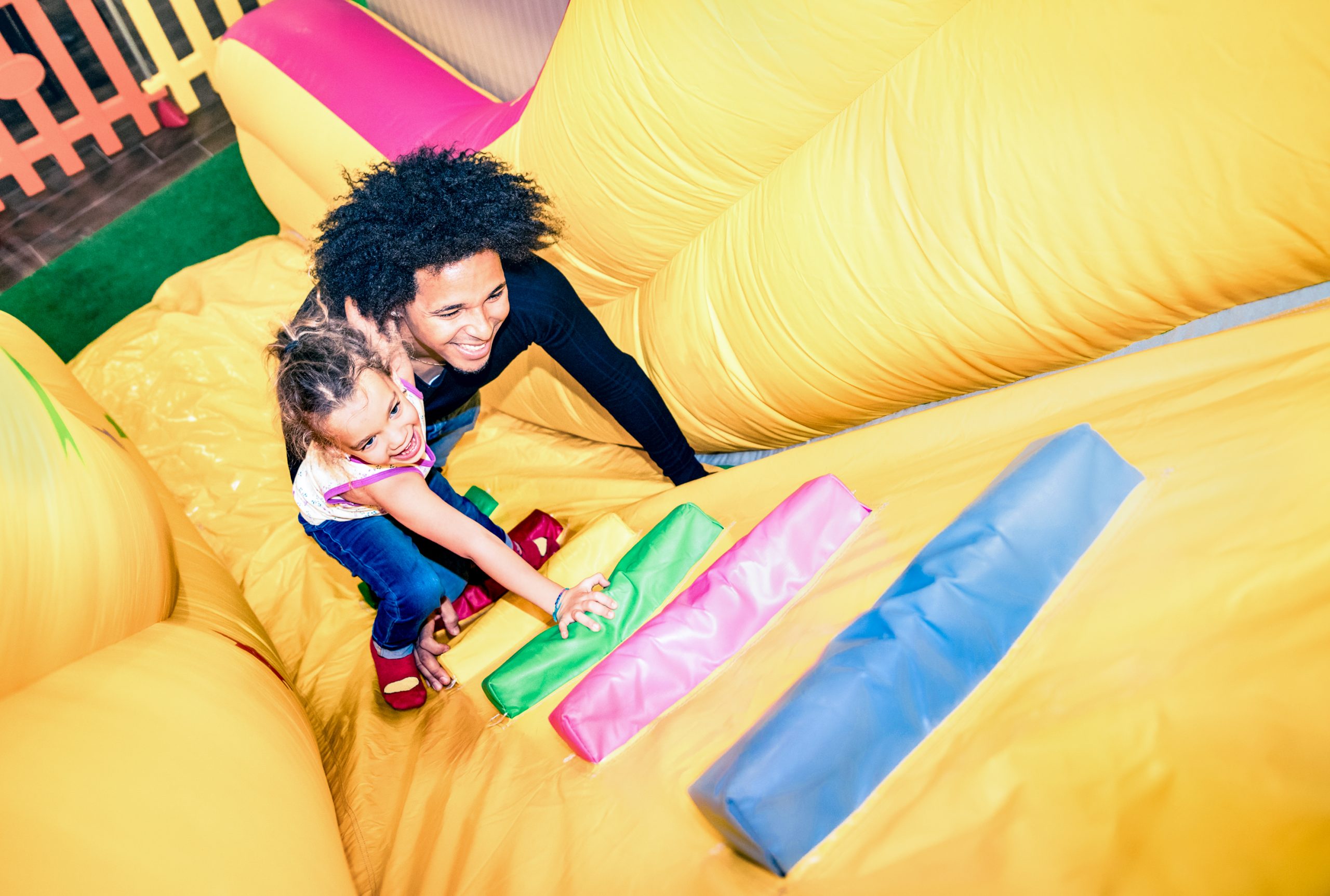 Latin american dad playing with mixed race daughter on inflatable slide at kindergarten playroom - Family concept with happy multiracial child and father having fun together at kids playground toyroom
